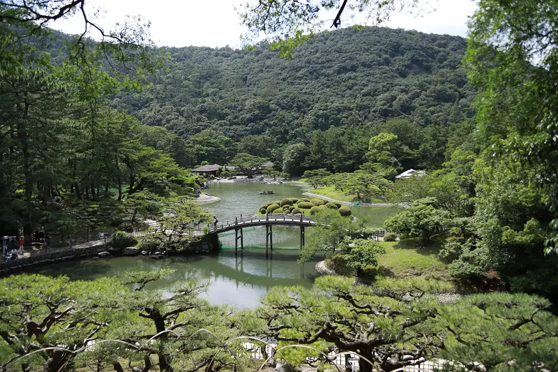 El puente arqueado sobre el estanque Sur del jardín Ritsurin, con pinos a lo largo de la orilla