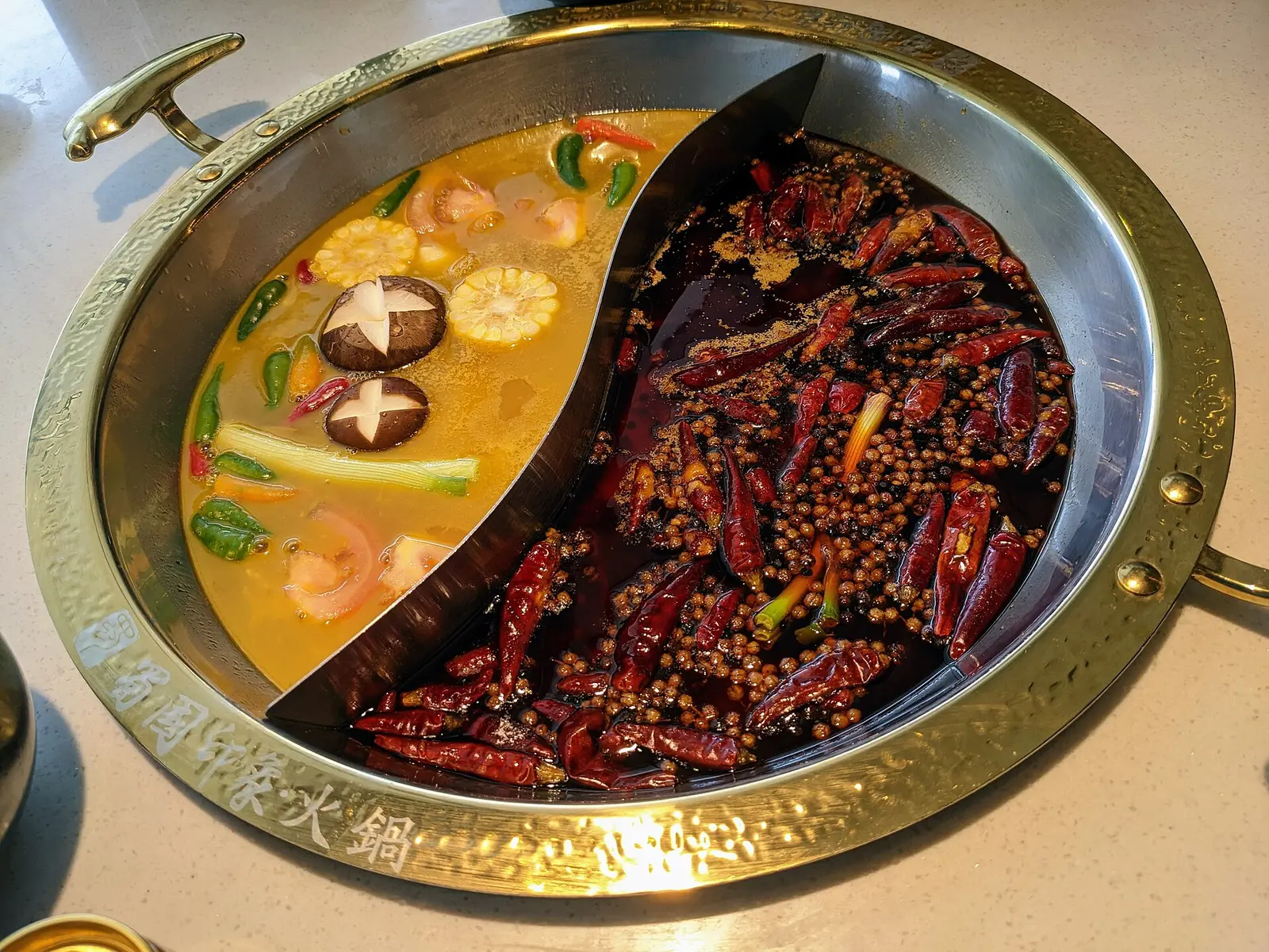 A Chengdu-style split pot, with pickled cabbage broth on the left and mala broth on the right; taken at a Sichuan hot pot restaurant in Johor Bahru, Malaysia, not in Chengdu